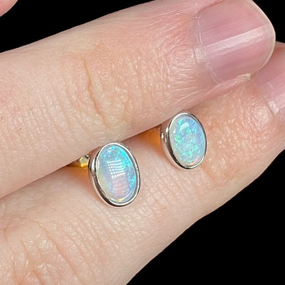 Angled view of blue crystal opal stud earrings in white gold, shown close-up held between two fingers.