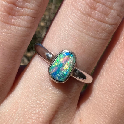 Close-up of multicolor blue and green Australian crystal opal ring made from silver, worn on hand in sunlight