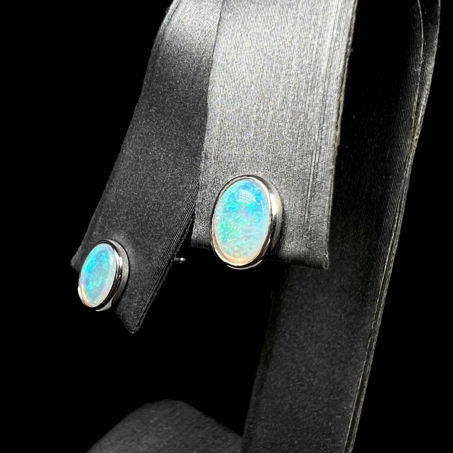 Angled view of subtle blue-green Australian crystal opal stud earrings in white gold bezels, shown on earring display.