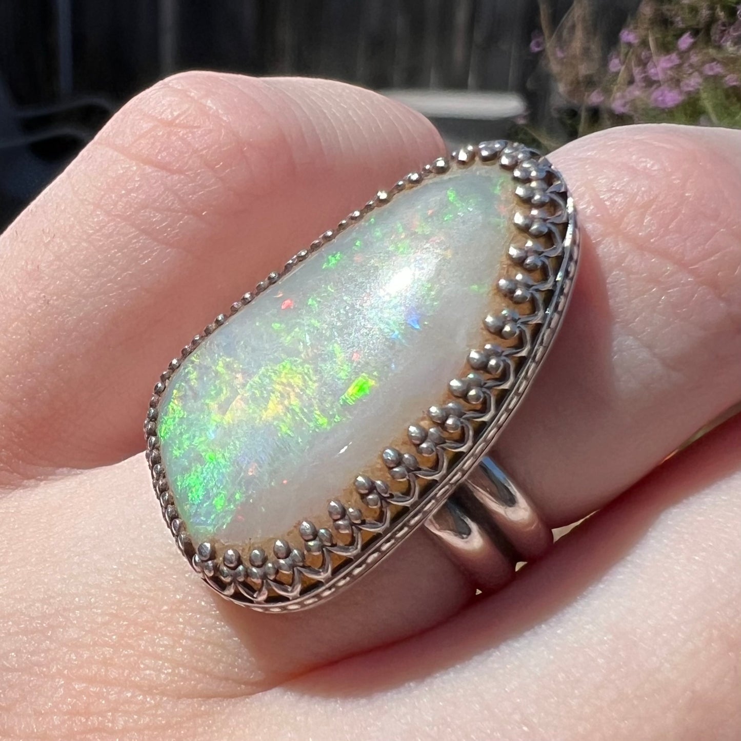 A Coober Pedy, Australian opal ring with a sterling silver crown design, shown close-up on a hand in natural light.  The opal has blue-green fire.