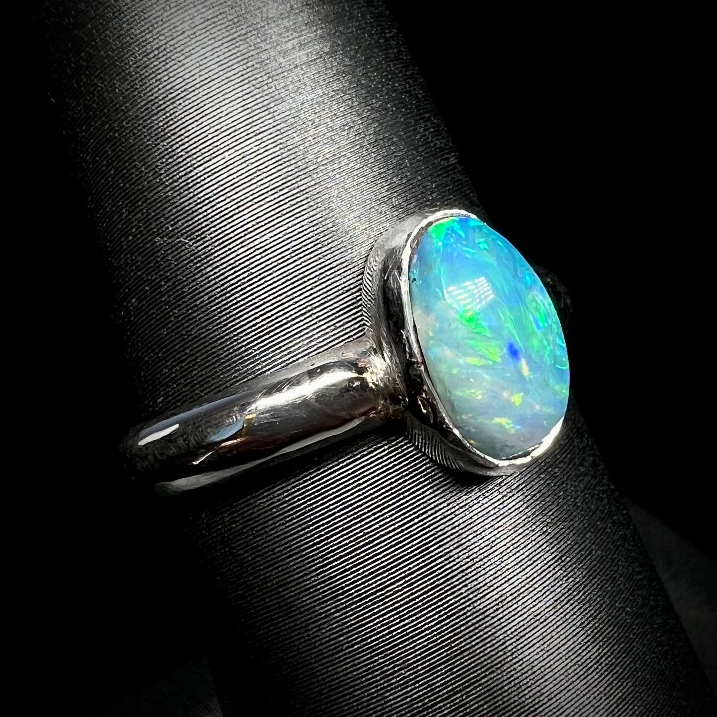 Angled view of a blue and green Australian opal ring in sterling silver, shown on a ring display against black backdrop.