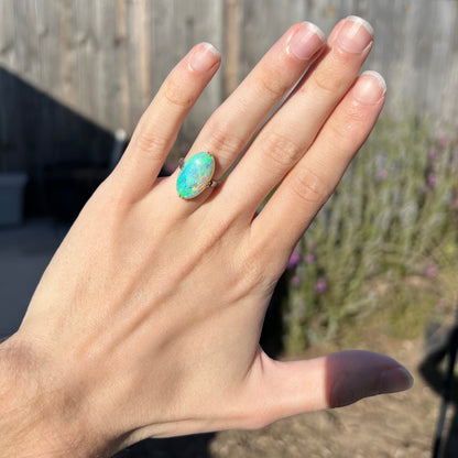 A platinum ring mounted with an oval cut Austalian crystal opal worn on a hand.  The opal is green and blue.