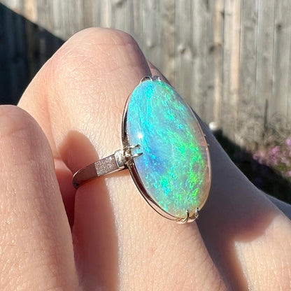 A blue-green opal ring showcased on a finger in the sunlight.  The opal is held by platinum prongs.