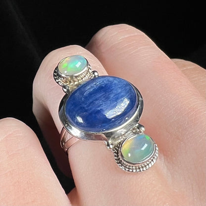 A blue kyanite cabochon ring with two Ethiopian opal accents, worn on a finger and shown at an angle.