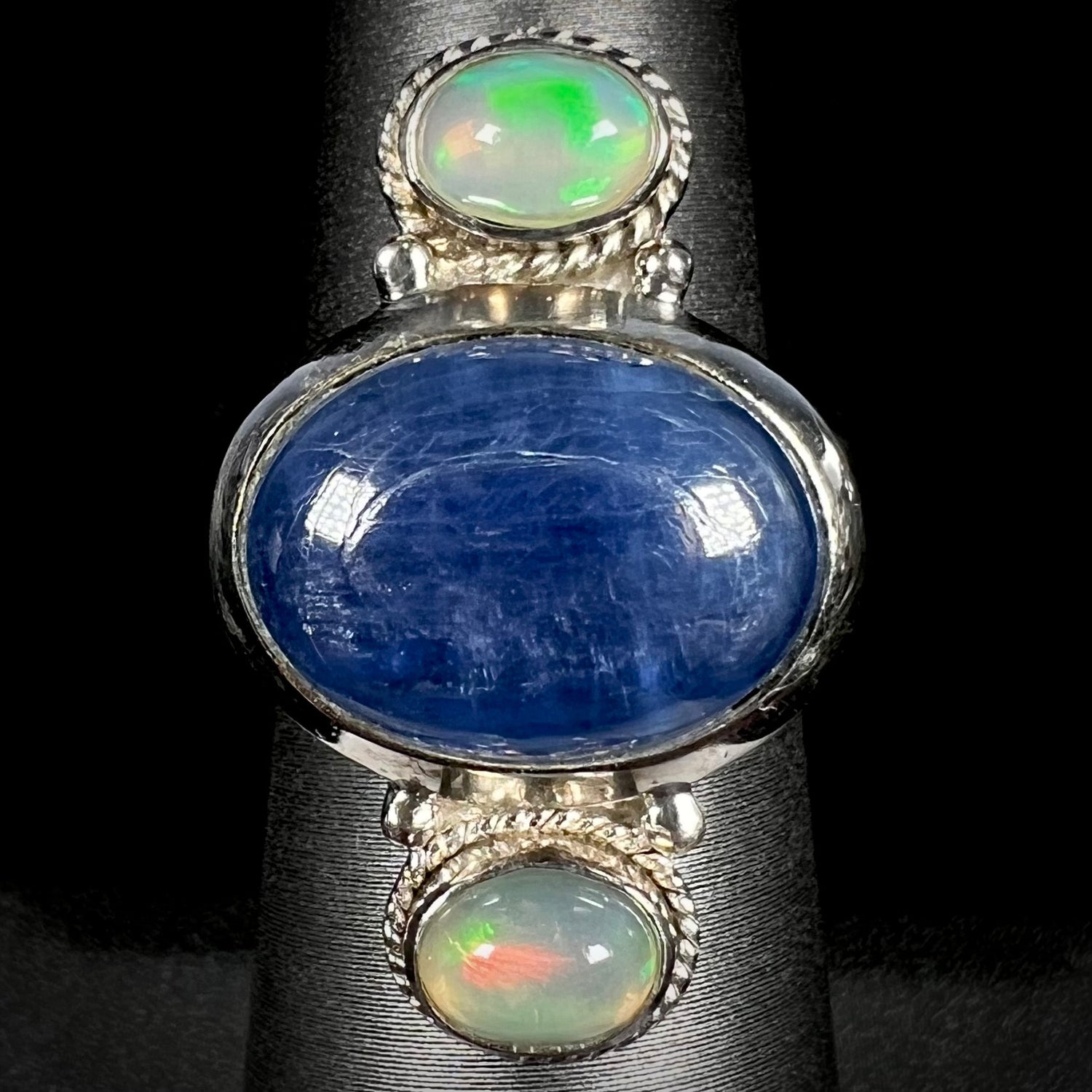 Front view of a blue kyanite cabochon and Ethiopian opal-accented silver ring against a black background.