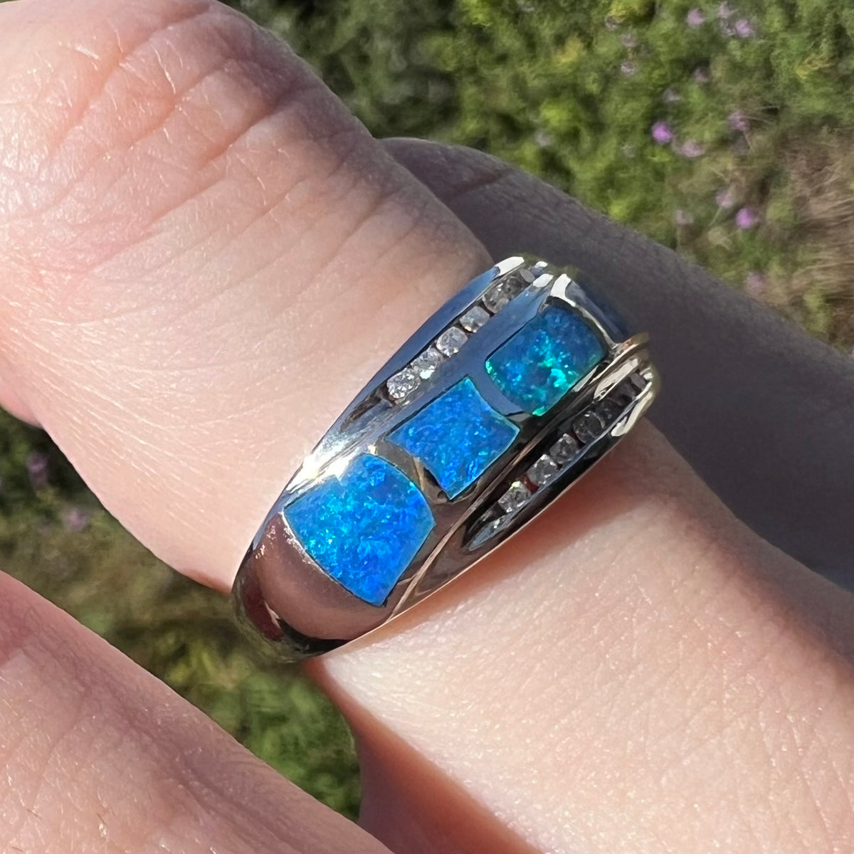 Australian blue opal inlay ring with channel set diamond accents in 14k white gold, worn on finger and viewed from close-up angle in sunlight