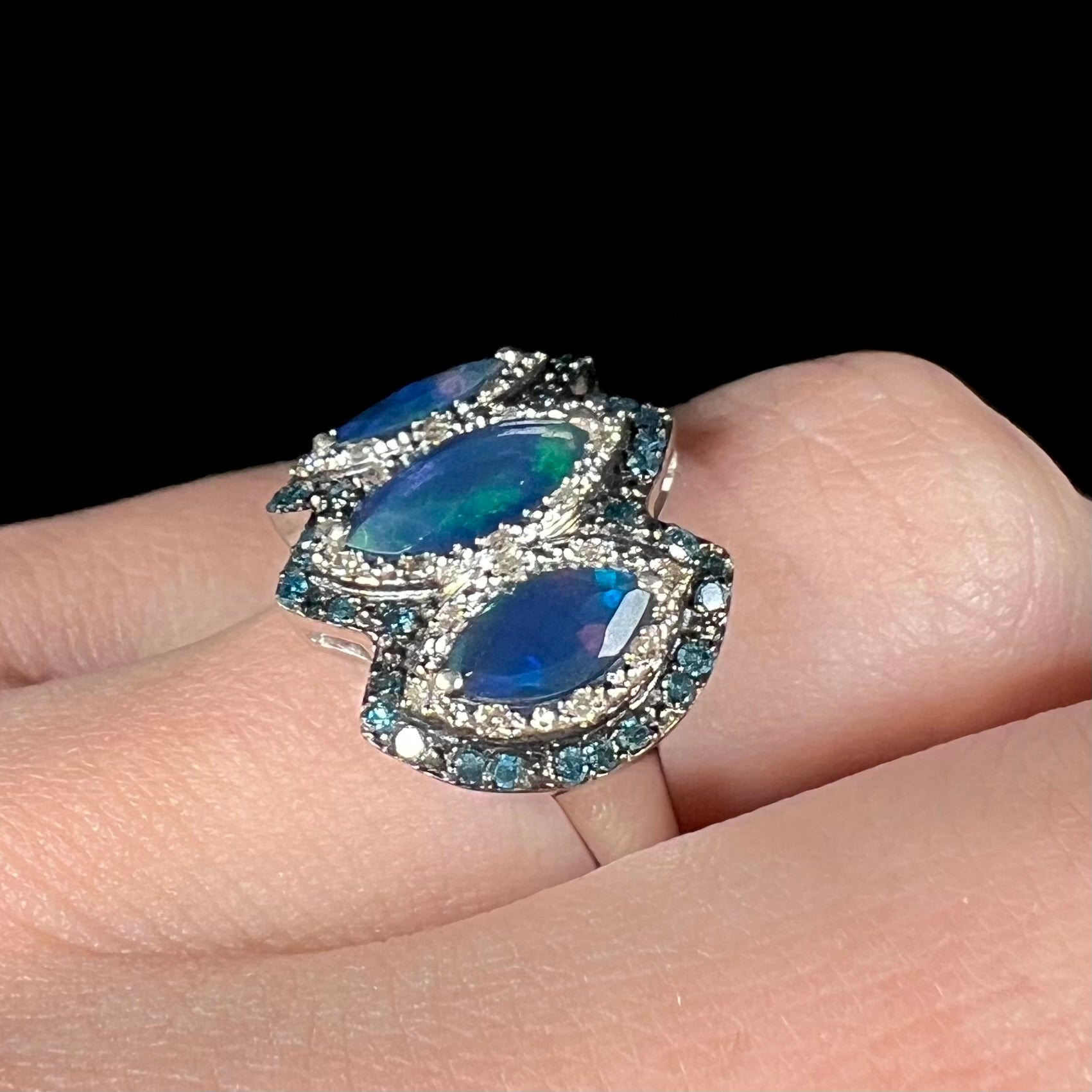 Angled view of a blue opal and diamond ring worn on a finger against a dark backdrop.
