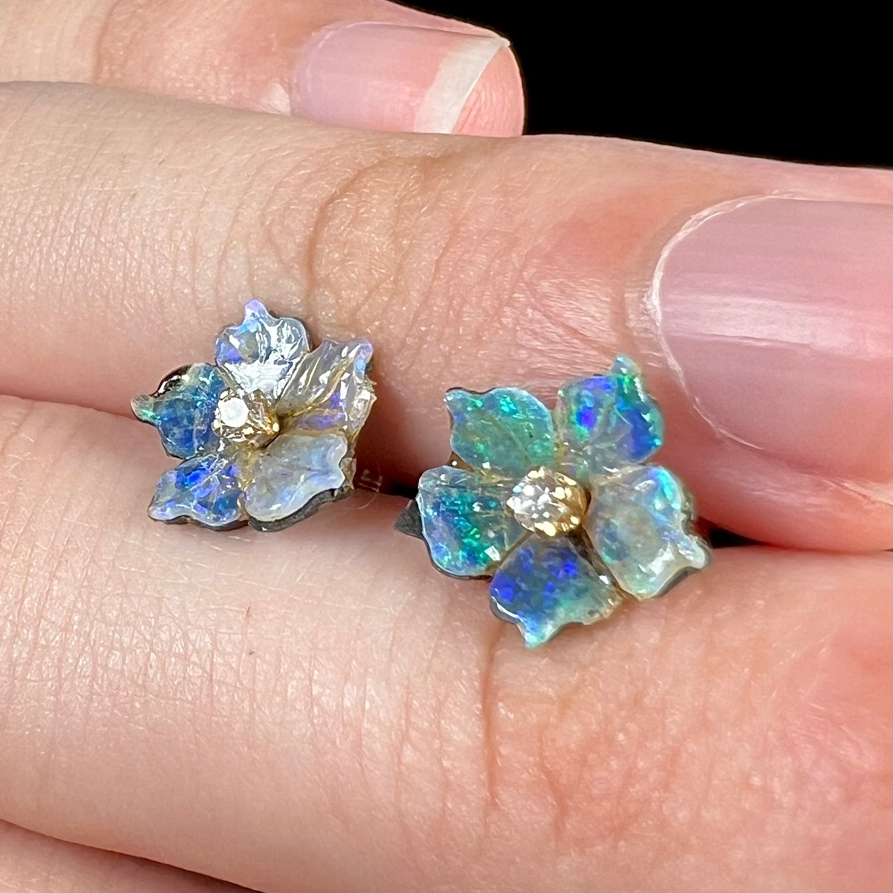 A pair of carved boulder opal doublet flower earring jackets with gold CZ studs shown close-up from an angle resting on a hand.