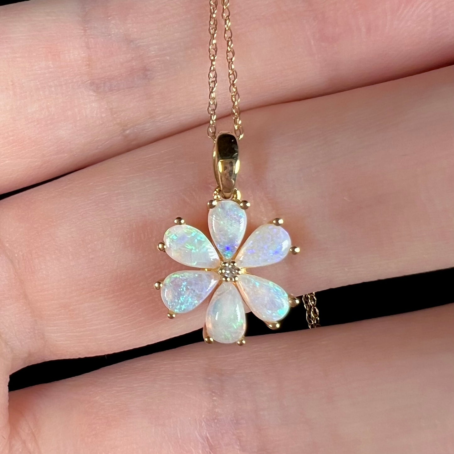Delicate blue flashes visible in opal flower pendant, held in hand