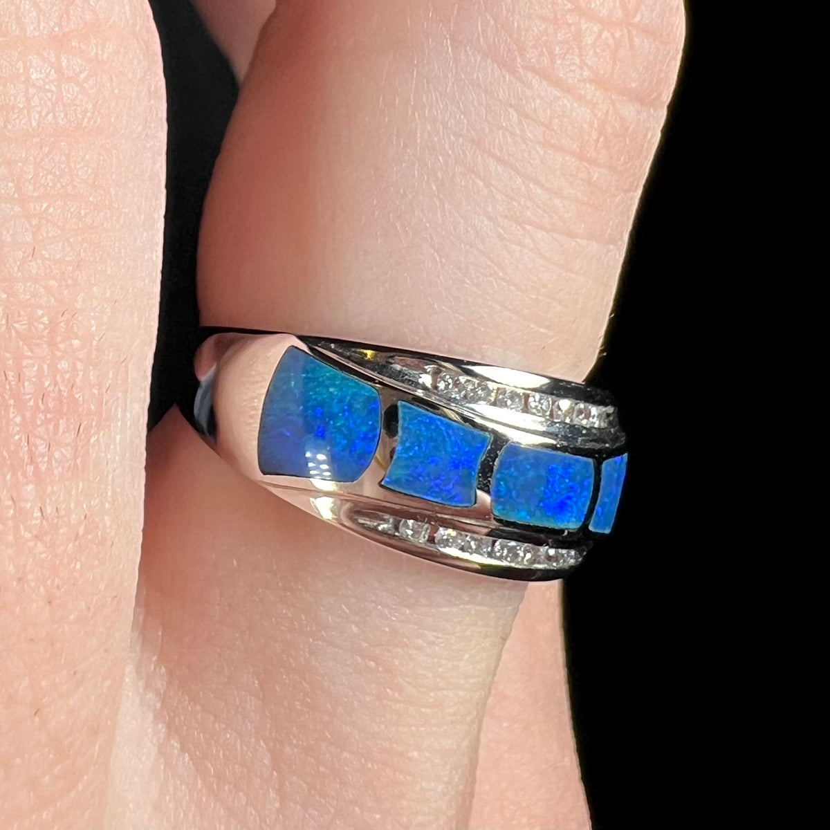 Blue Australian opal inlay ring in 14k white gold with diamond accents shown close-up from angle on a finger