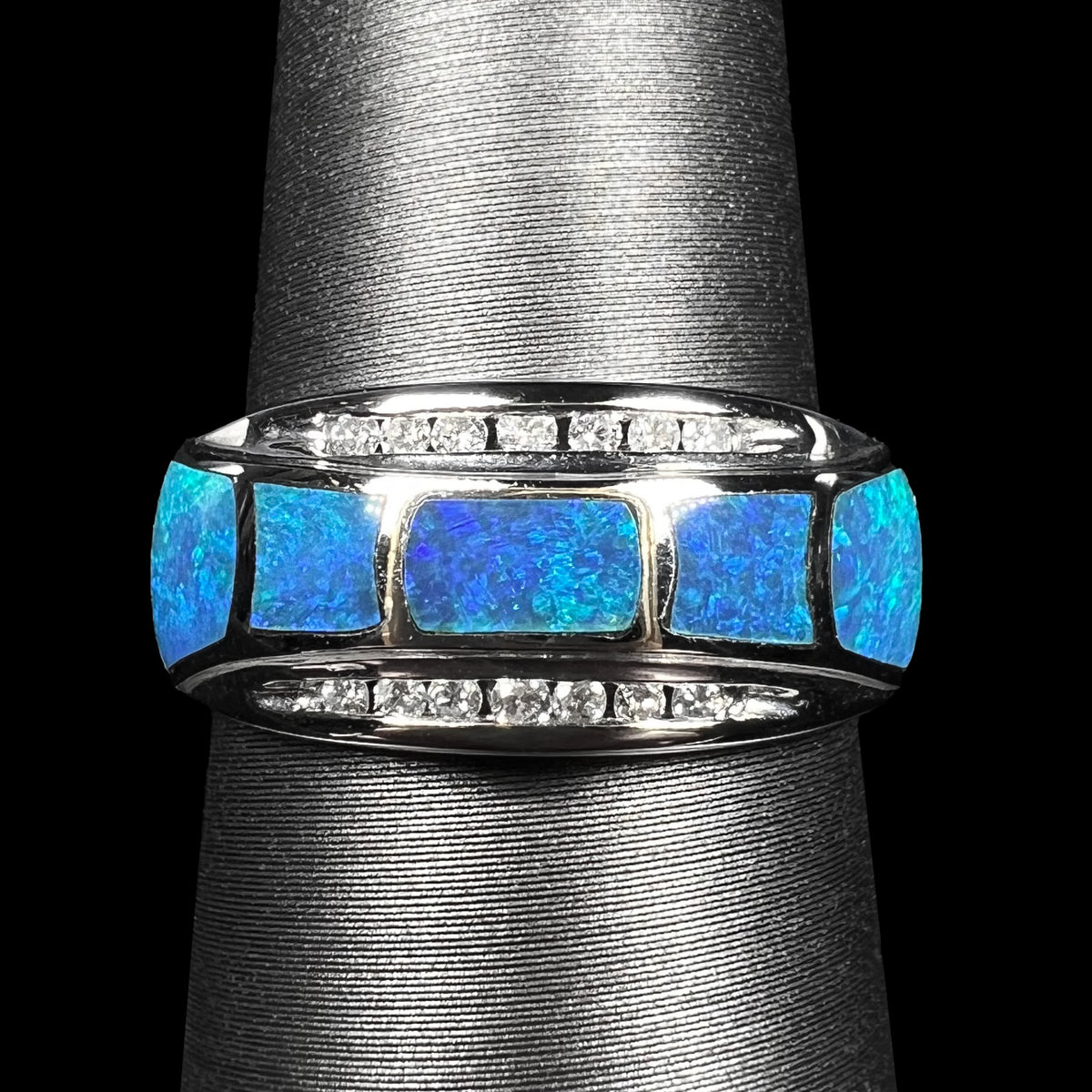 Close-up of 14k white gold ring inlaid with five blue Australian opals, accented by two channels of diamonds, shown on ring display