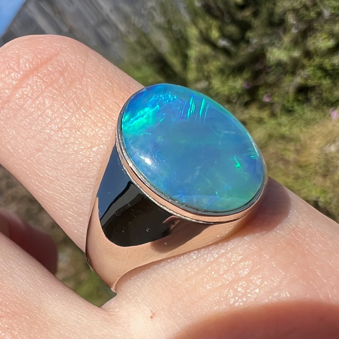 White gold men's ring set with blue Australian crystal opal, worn on finger in sunlight