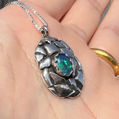 A unisex sterling silver pinecone-inspired opal triplet necklace shown in the sunlight from an angle.