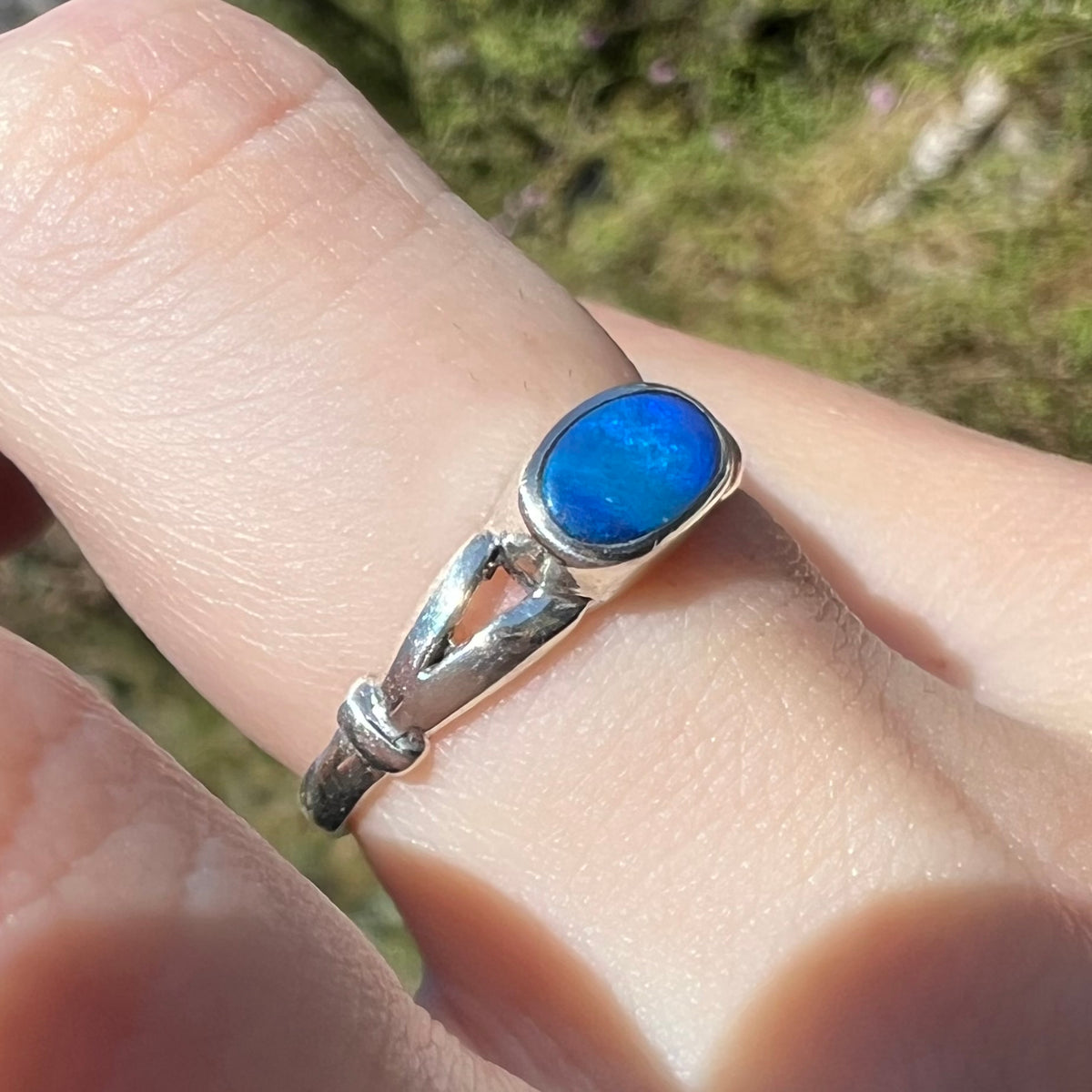 Angled close-up of blue opal solitaire ring in silver, worn on finger in sunlight