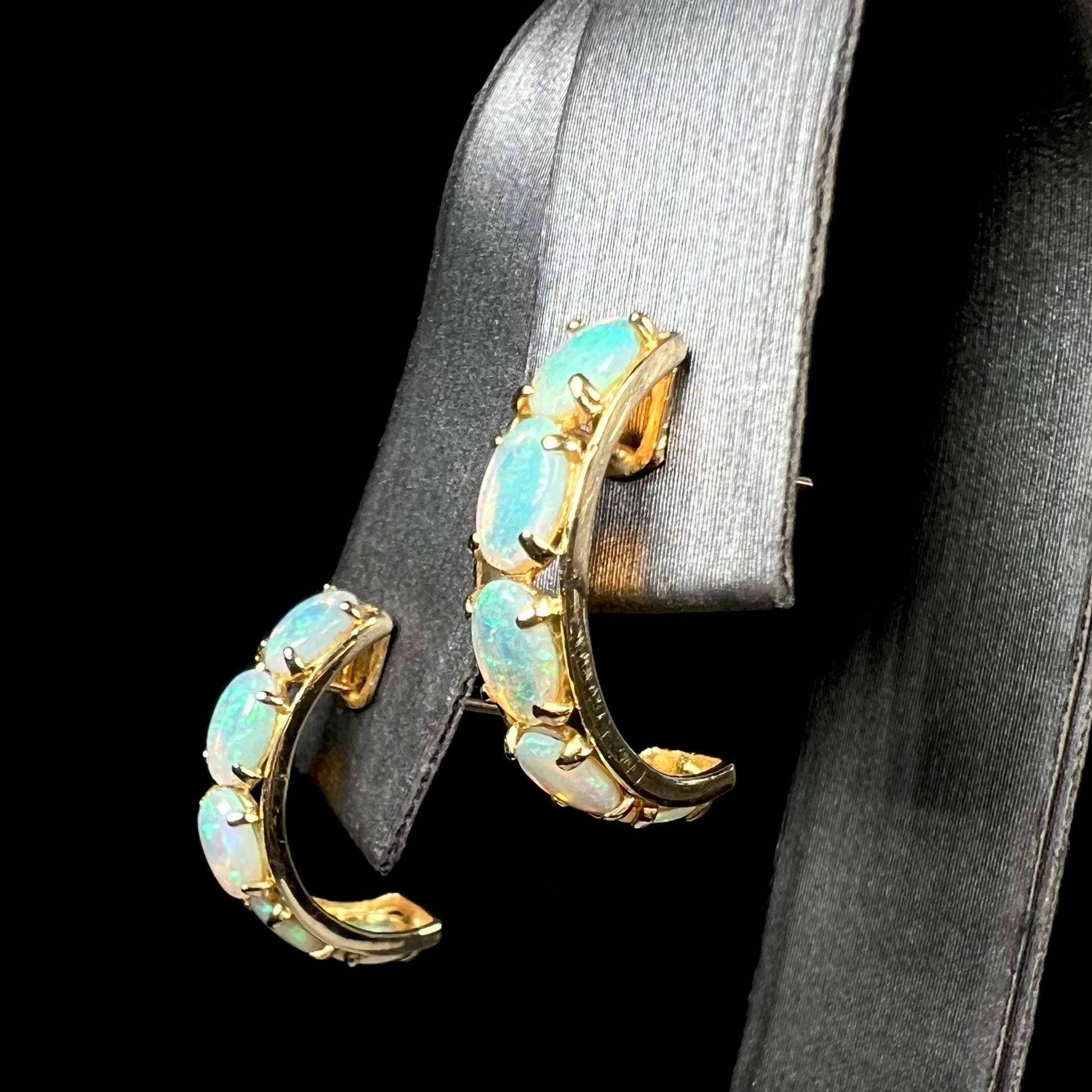 Angled view of five-stone yellow gold opal semi-hoop earrings shown on an earring display against a black background.