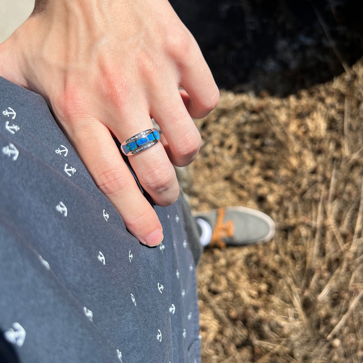Person's hand resting on hip in sunlight wearing a white gold ring inlaid with five pieces of blue opal, accented by two rows of channel set diamonds