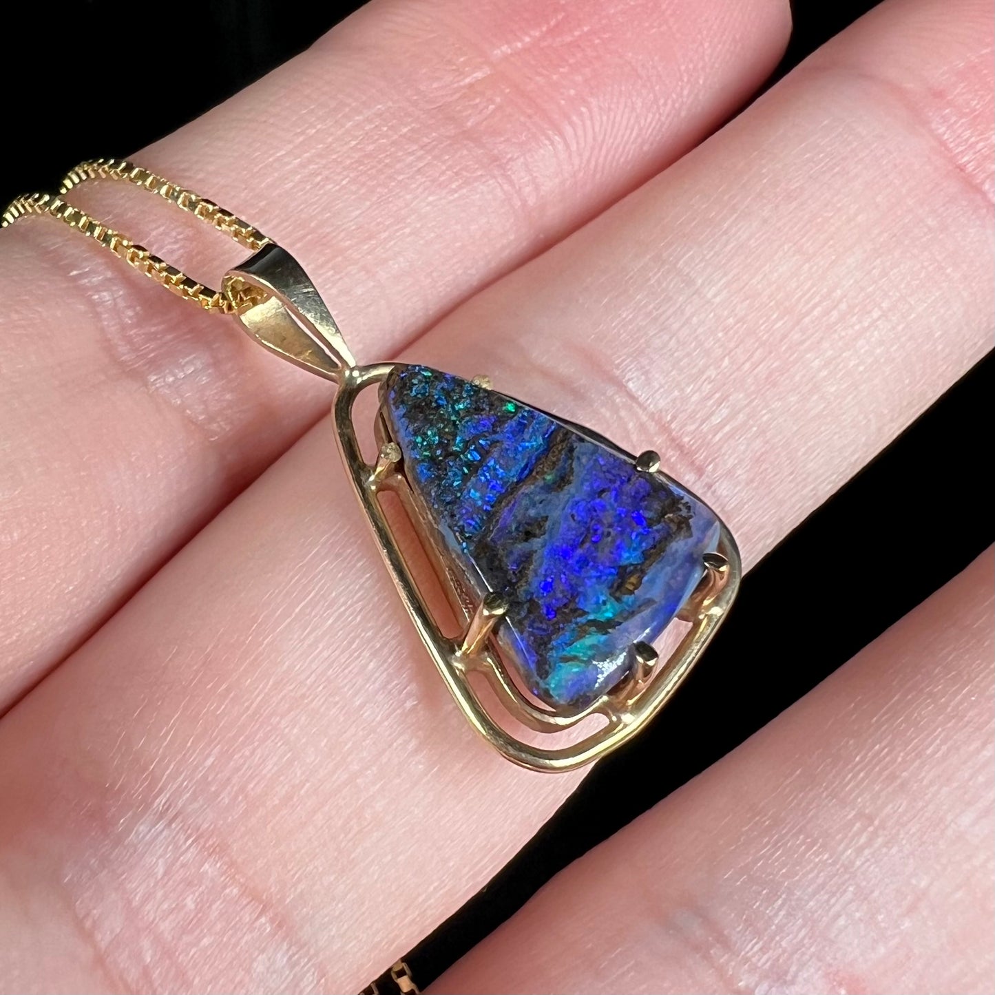 Angled close-up of a dainty Duck Creek opalized wood necklace in 9k gold, shown in a hand.