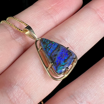 Angled close-up of a dainty Duck Creek opalized wood necklace in 9k gold, shown in a hand.