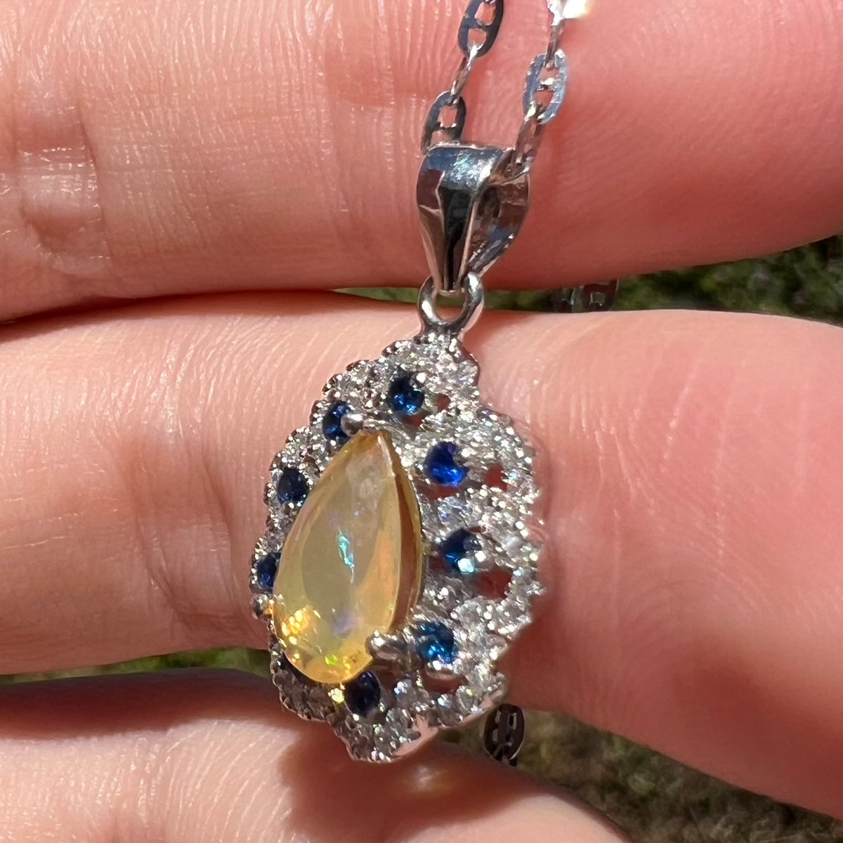 Side view of blue sapphire and Ethiopian opal pendant in silver, held in hand under sunlight