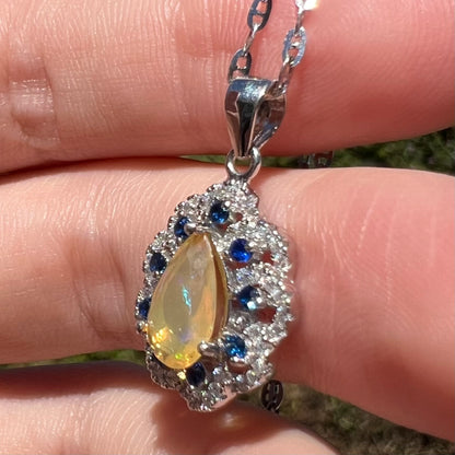 Side view of blue sapphire and Ethiopian opal pendant in silver, held in hand under sunlight