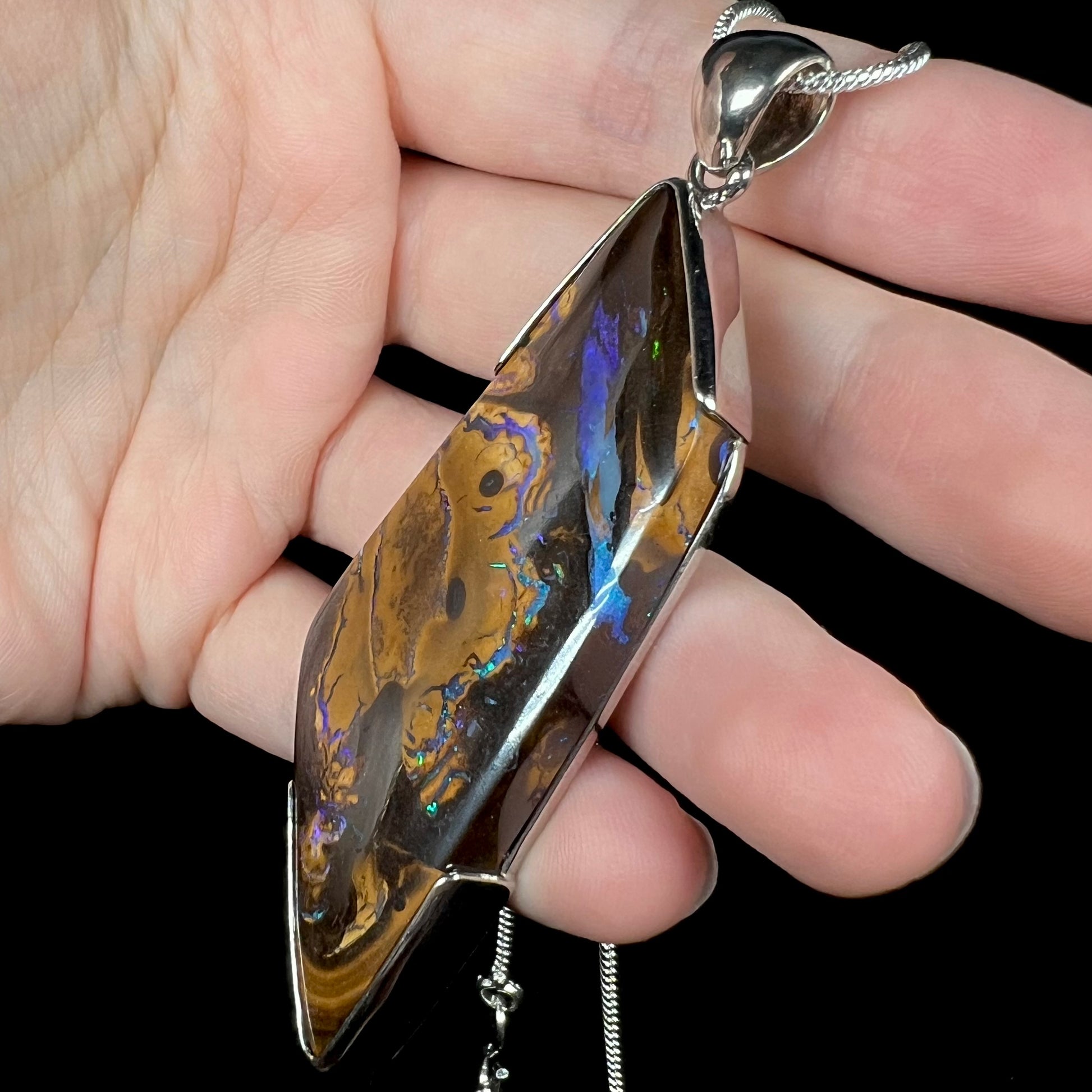 Side view of blue-striped Australian boulder opal pendant in silver, held in hand