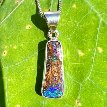 An elongated shaped natural boulder opal necklace in sterling silver.  The opal flashes bright blue and green colors.