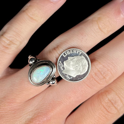 A Boho opal ring with green and blue color play, worn on a hand next to a dime coin.