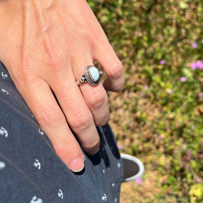 A silver Boho opal ring worn on a hand that's resting on the model's hip in the sunlight.