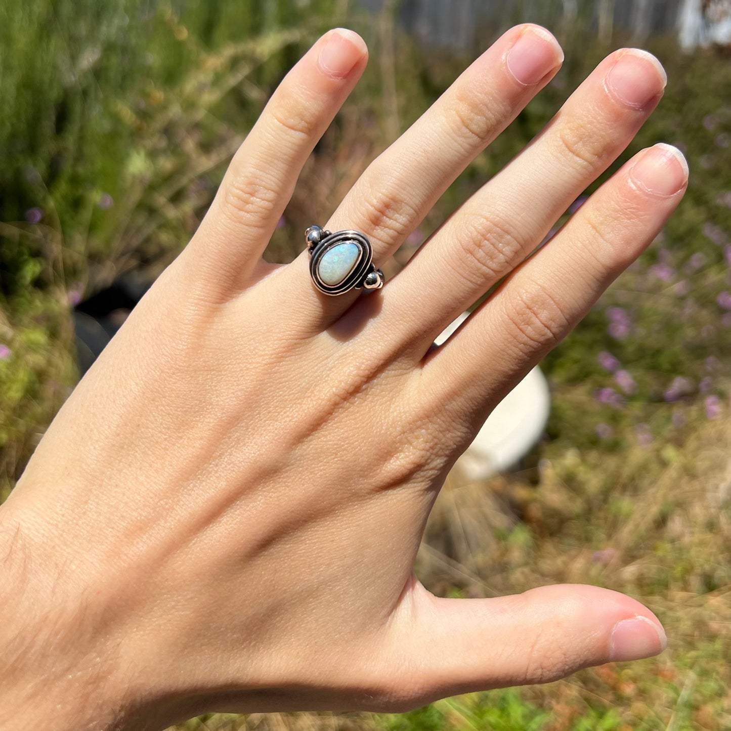 A handmade Boho-style sterling silver opal ring set with an Australian opal, worn on a hand in sunlight.