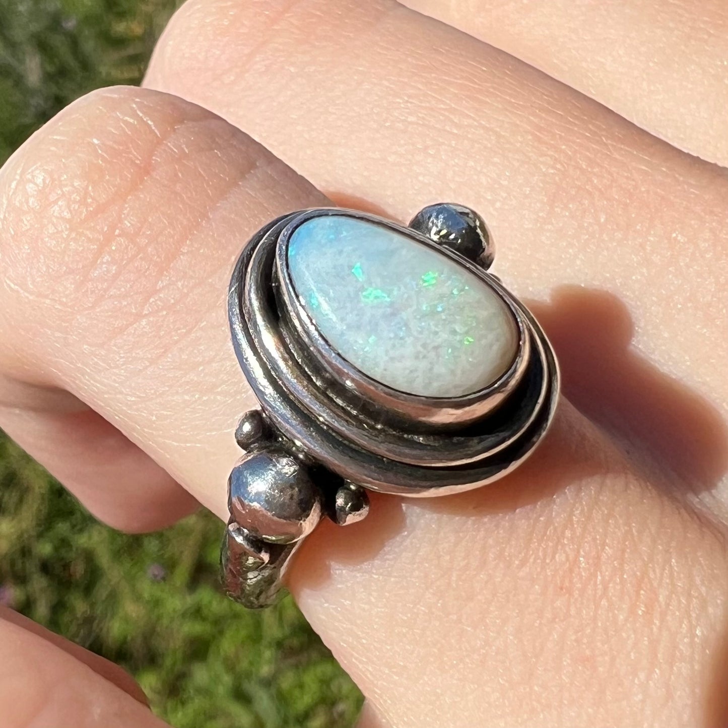 A handmade Boho-style sterling silver opal ring set with an Australian opal, worn on a finger at an angle in sunlight.