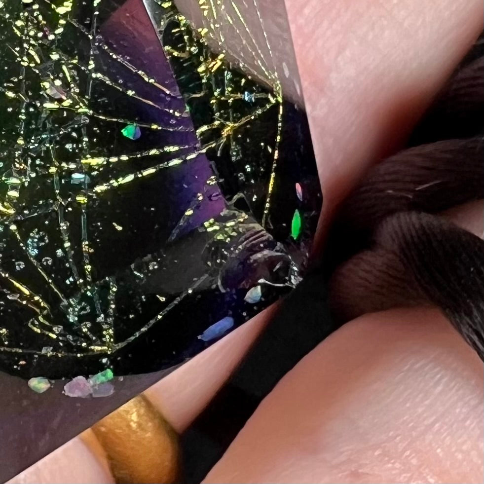 Zoomed in close-up of a damaged chipped facet on a purple borosilicate glass and lab-created opal pendant.