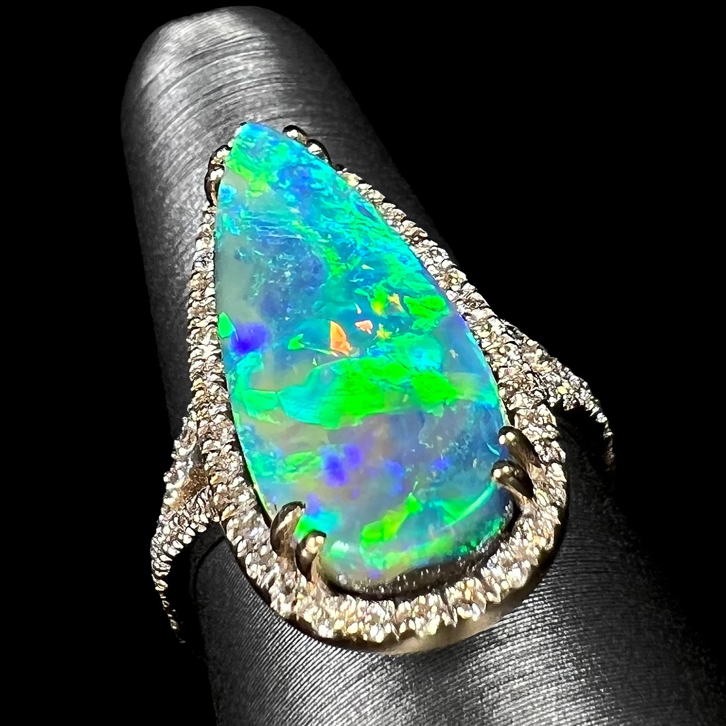 Angled up-facing view of a boulder opal engagement ring showing green and blue directional fire on a ring display.