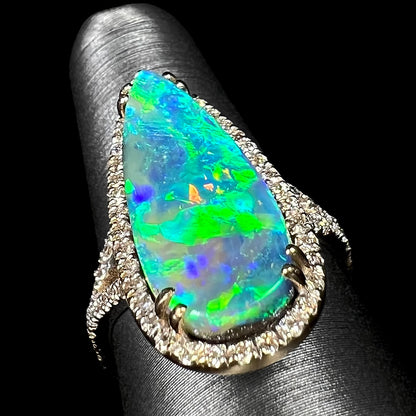 Angled up-facing view of a boulder opal engagement ring showing green and blue directional fire on a ring display.