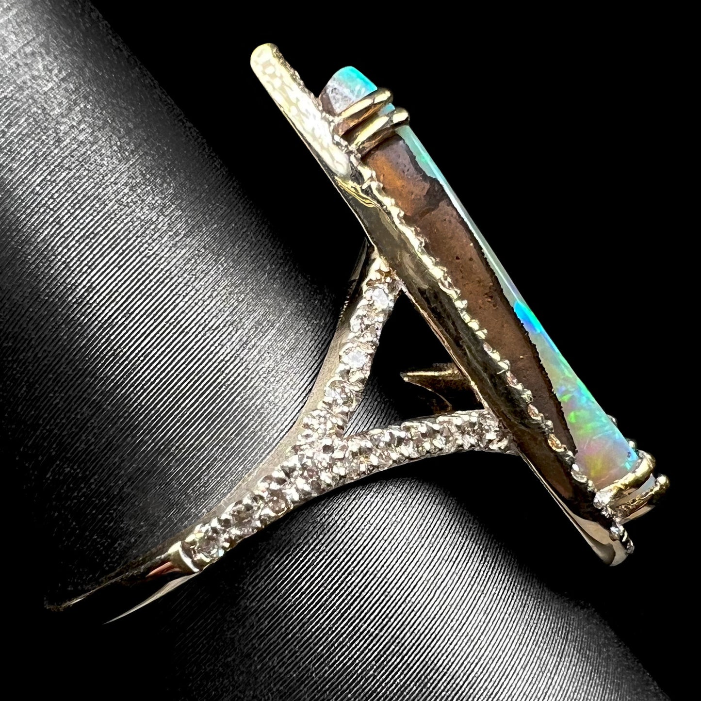 Side profile view of a boulder opal ring with a diamond pave split shank design, shown on a ring display.