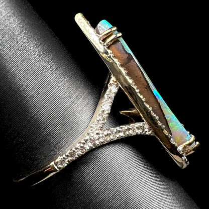 Side profile view of a boulder opal ring with a diamond pave split shank design, shown on a ring display.