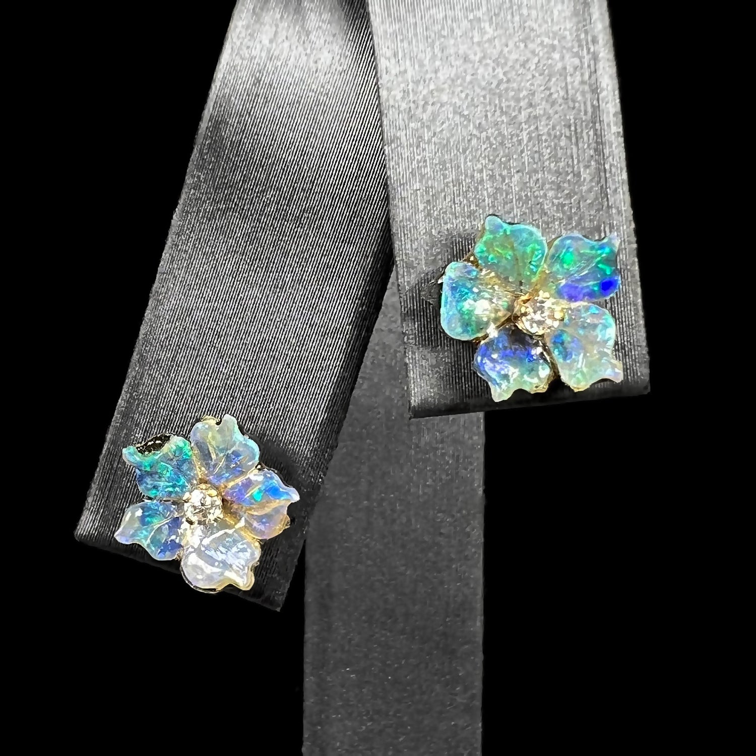 A pair of carved boulder opal doublet flower earring jackets with gold CZ studs shown from the front view on an earring display.