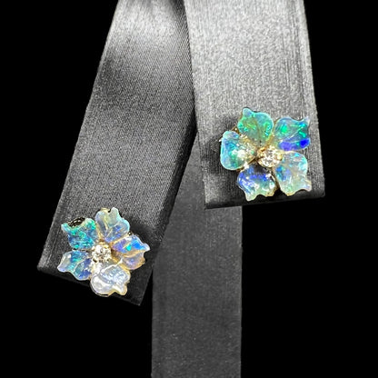 A pair of carved boulder opal doublet flower earring jackets with gold CZ studs shown from the front view on an earring display.