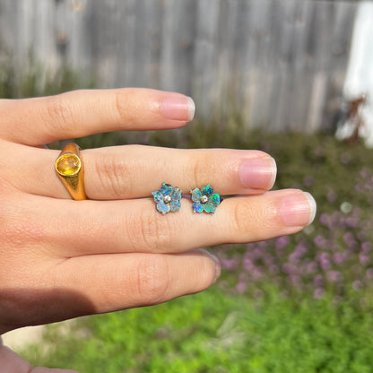 A pair of carved boulder opal doublet flower earring jackets with gold CZ studs shown resting on a hand in sunlight against an outdoor backdrop.