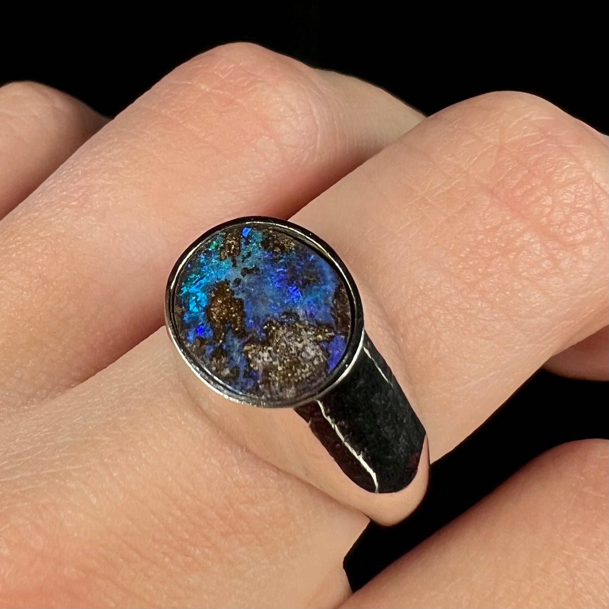 A stainless steel men's Australian boulder opal ring with blue color play shown angled close-up on a finger.