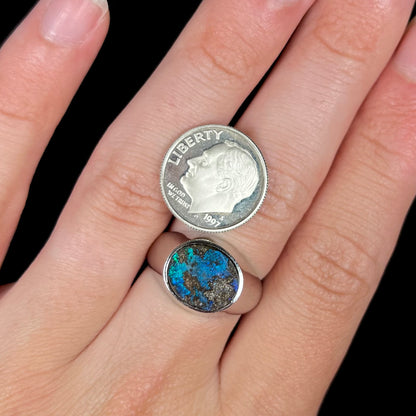 A stainless steel men's Australian boulder opal ring with blue color play shown on a finger with a dime coin.