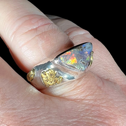 Man's size 12 finger shown from an angle wearing a gold nugget-accented Australian boulder opal solitaire ring.  The opal has red and orange play of color.