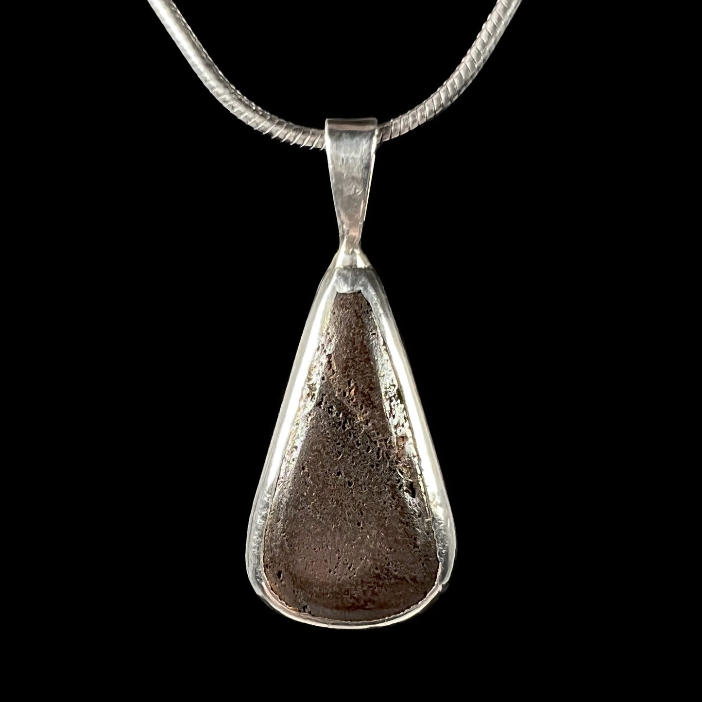 The back of a boulder opal necklace, revealing its brown ironstone matrix in an open sterling silver frame.