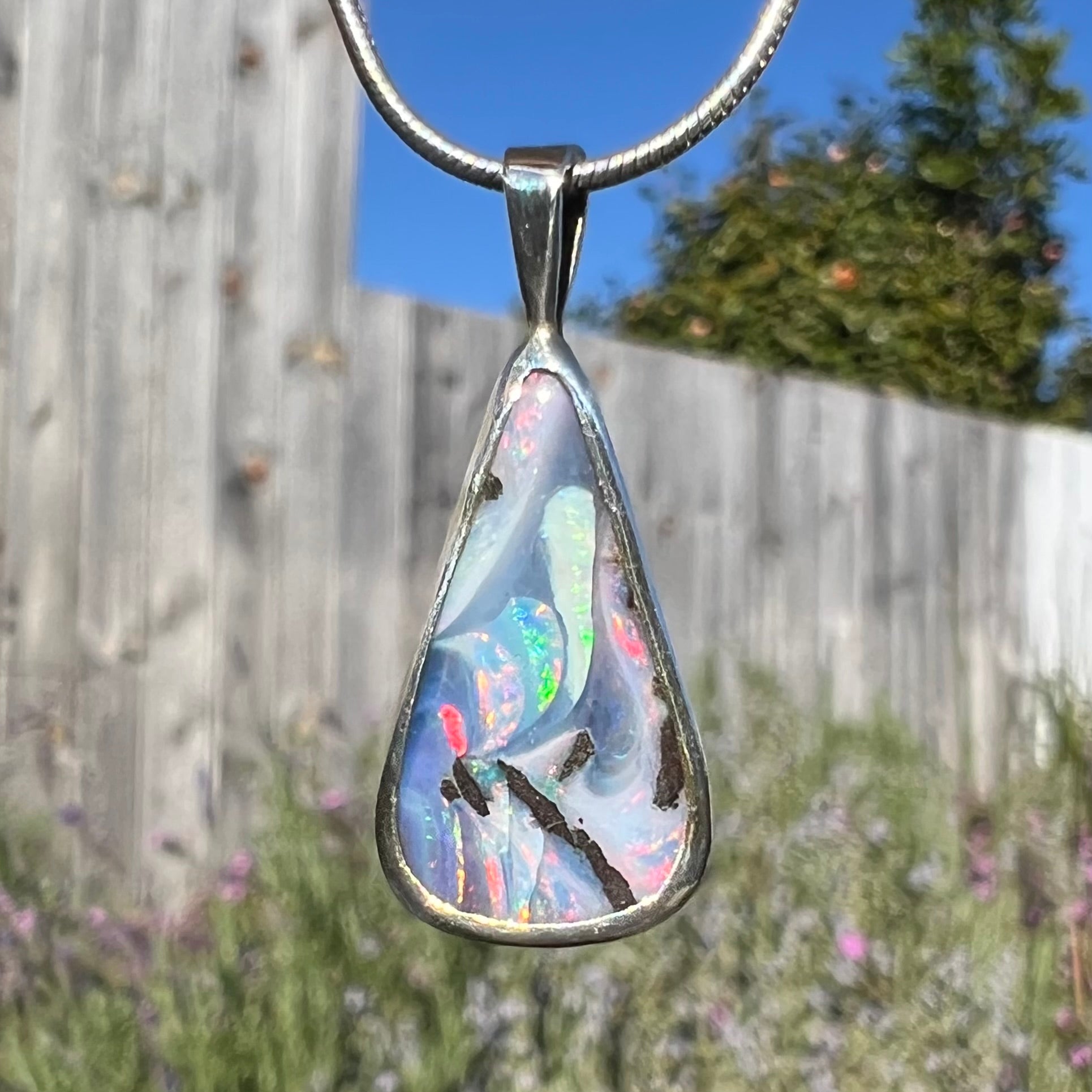 A macro close-up of a boulder opal necklace in natural sunlight, with intensified color play.