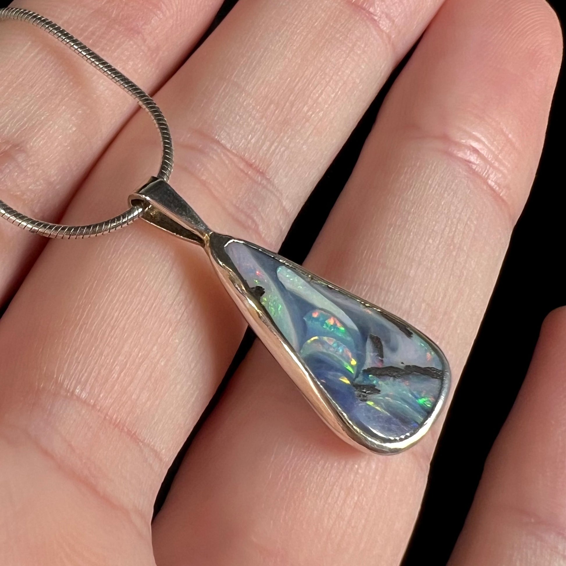 An angled macro close-up of a boulder opal necklace, revealing flashes of green fire.