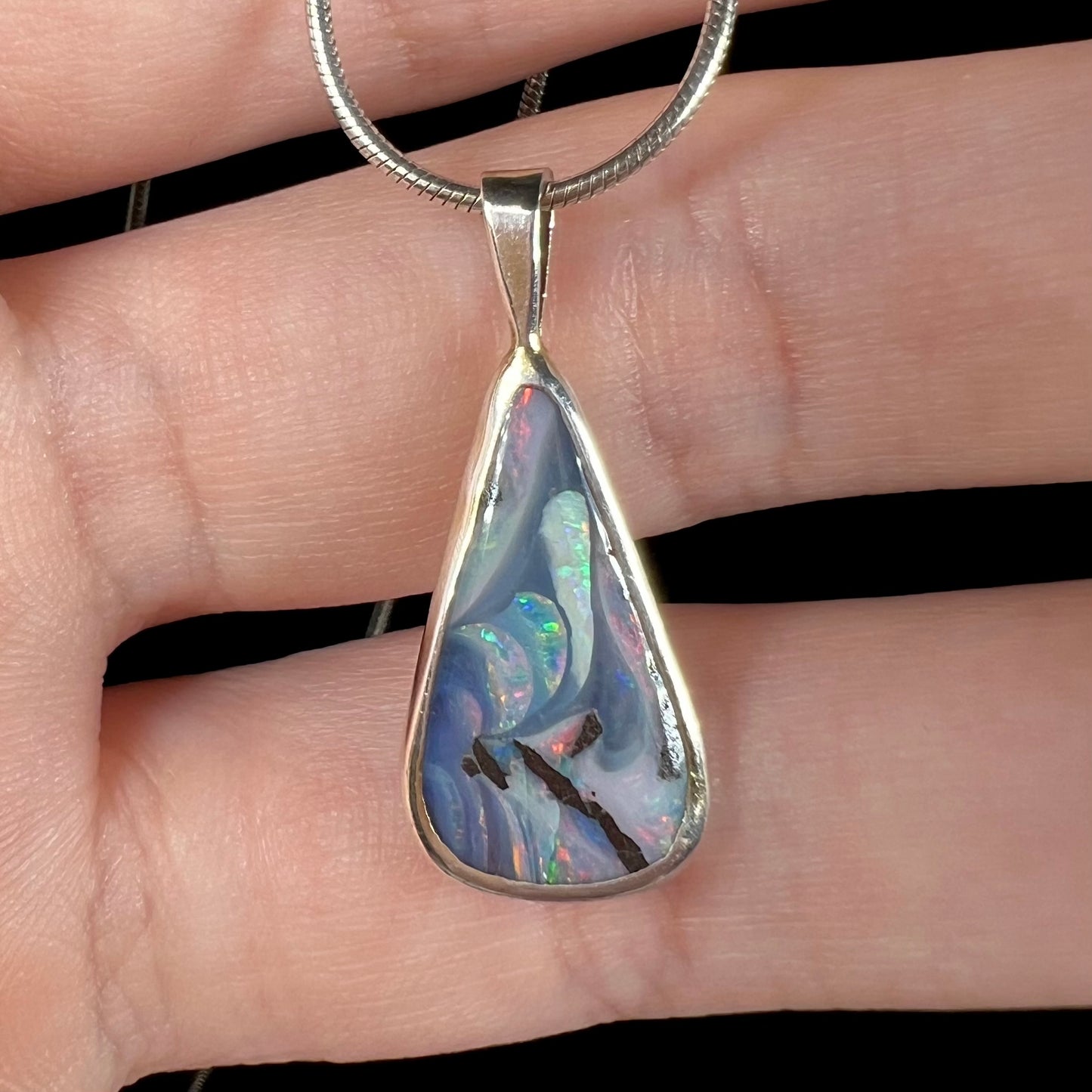 A macro close-up of a boulder opal necklace on fingers, showing its intricate pattern and depth of color.