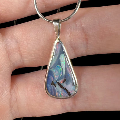 A macro close-up of a boulder opal necklace on fingers, showing its intricate pattern and depth of color.