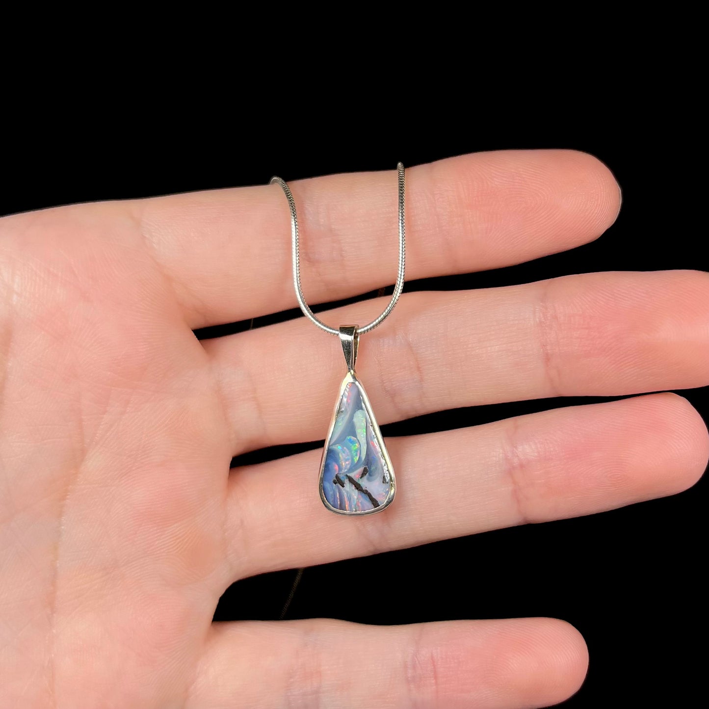 A boulder opal necklace resting on fingers against a black background.