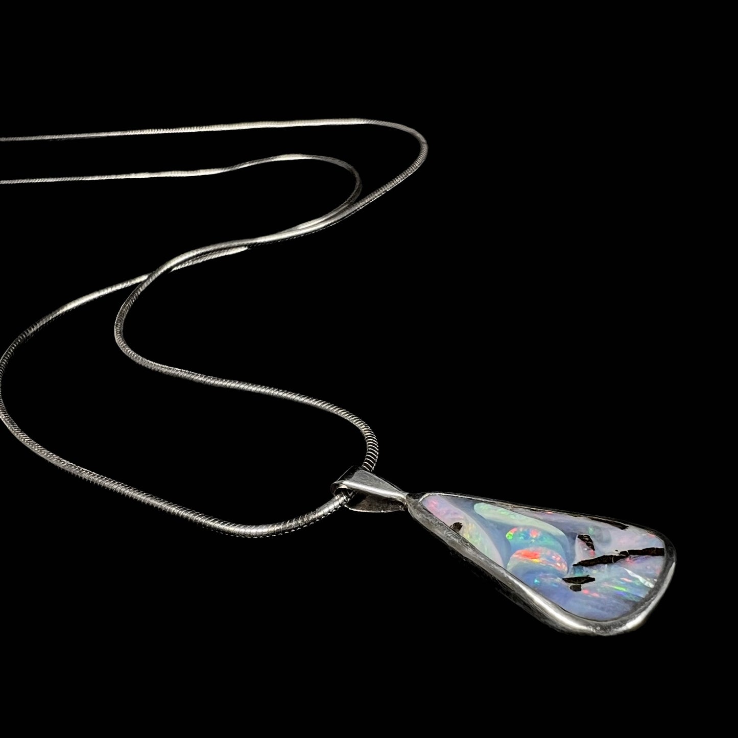 An angled view of a boulder opal necklace lying on a black background, highlighting its swirling color patterns.