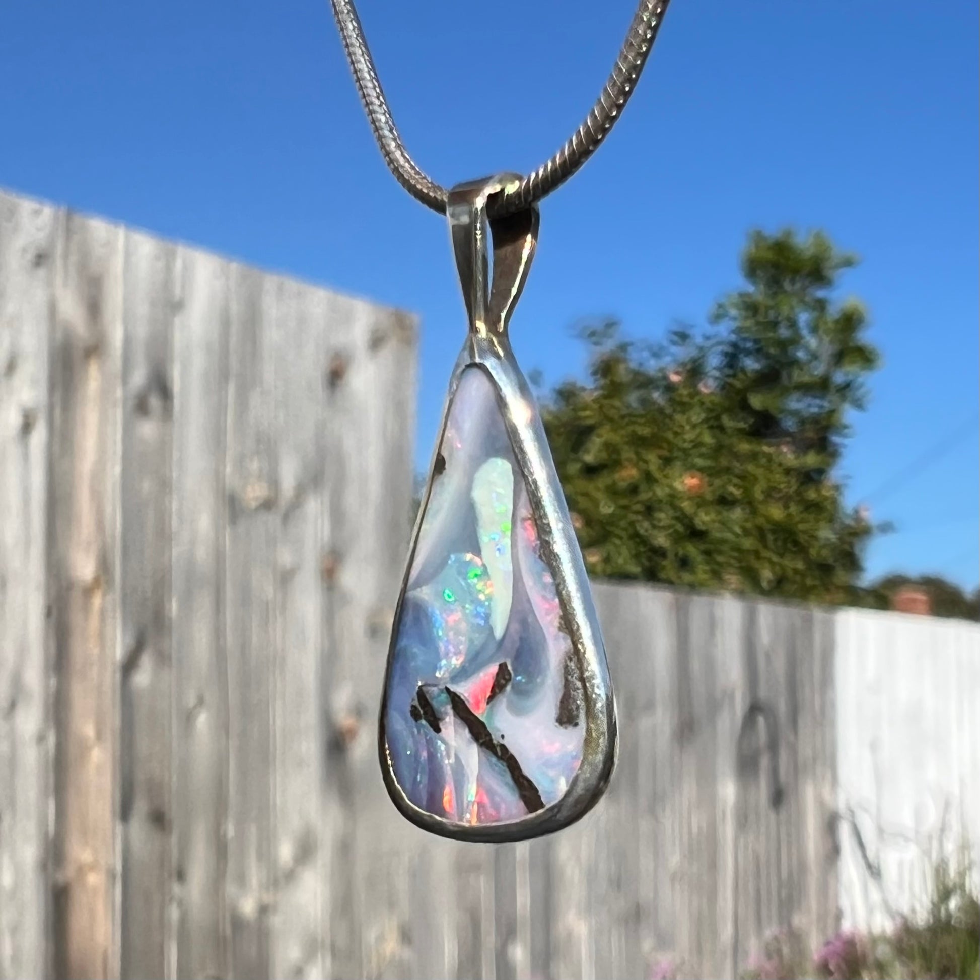 A boulder opal necklace viewed from the opposite side in direct sunlight, with vibrant opal fire.