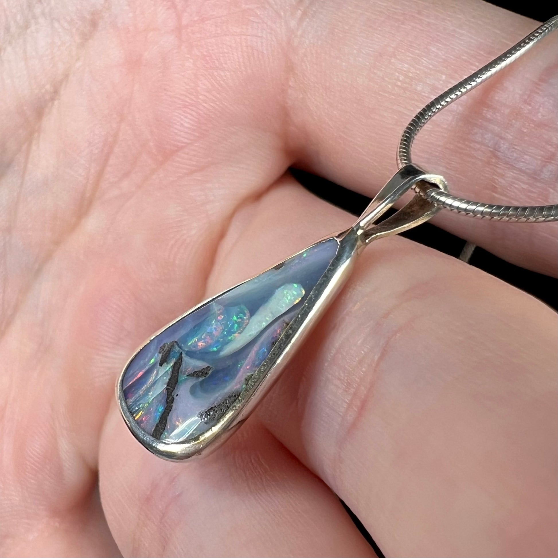 A side view of a boulder opal necklace, where subtle pink and blue flashes are visible in different lighting.